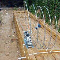 Volt Customs -Maksym Ruban - Niezamontowany, metalowy napęd do bramy na palecie drewnianych desek, widok z boku, zarośnięte tło.