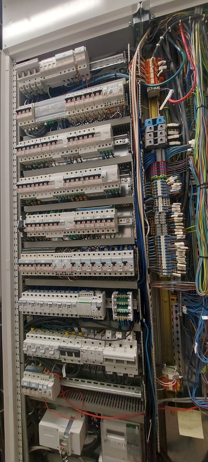 Rozdzielnica elektryczna z licznymi zabezpieczeniami nadprądowymi, różnicowoprądowymi i przewodami w kolorowej izolacji, zamontowana w metalowej szafie.