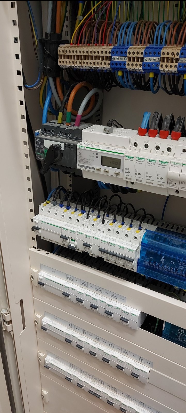 Rozdzielnica elektryczna w szafie z widocznymi bezpiecznikami, przewodami i wyłącznikiem głównym, marki Schneider Electric.