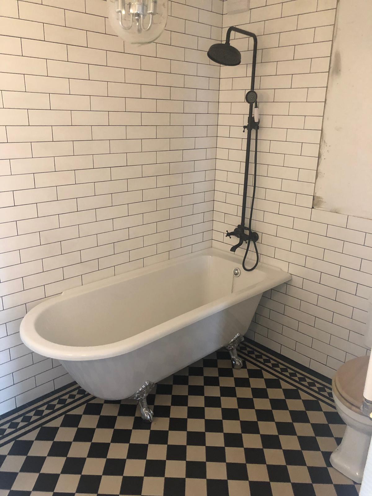 Biała wanna wolnostojąca na lwich nóżkach, czarno-biała szachownica na podłodze, białe kafelki na ścianach z czarną fugą, czarna bateria prysznicowa retro.