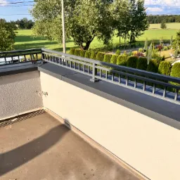 Barierka balkonu z widokiem na zielony krajobraz, na ścianie widoczne okablowanie