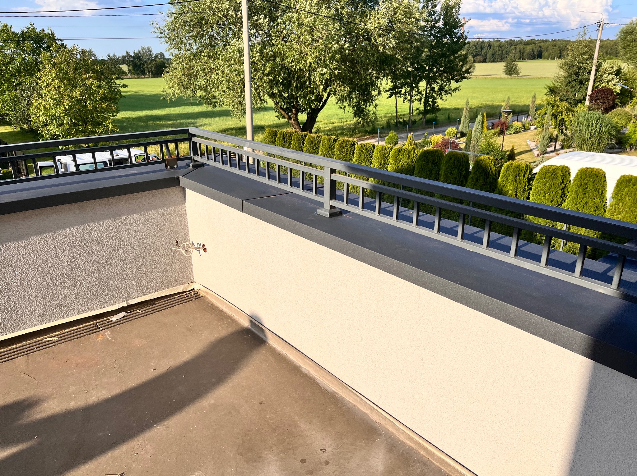 Barierka balkonu z widokiem na zielony krajobraz, na ścianie widoczne okablowanie