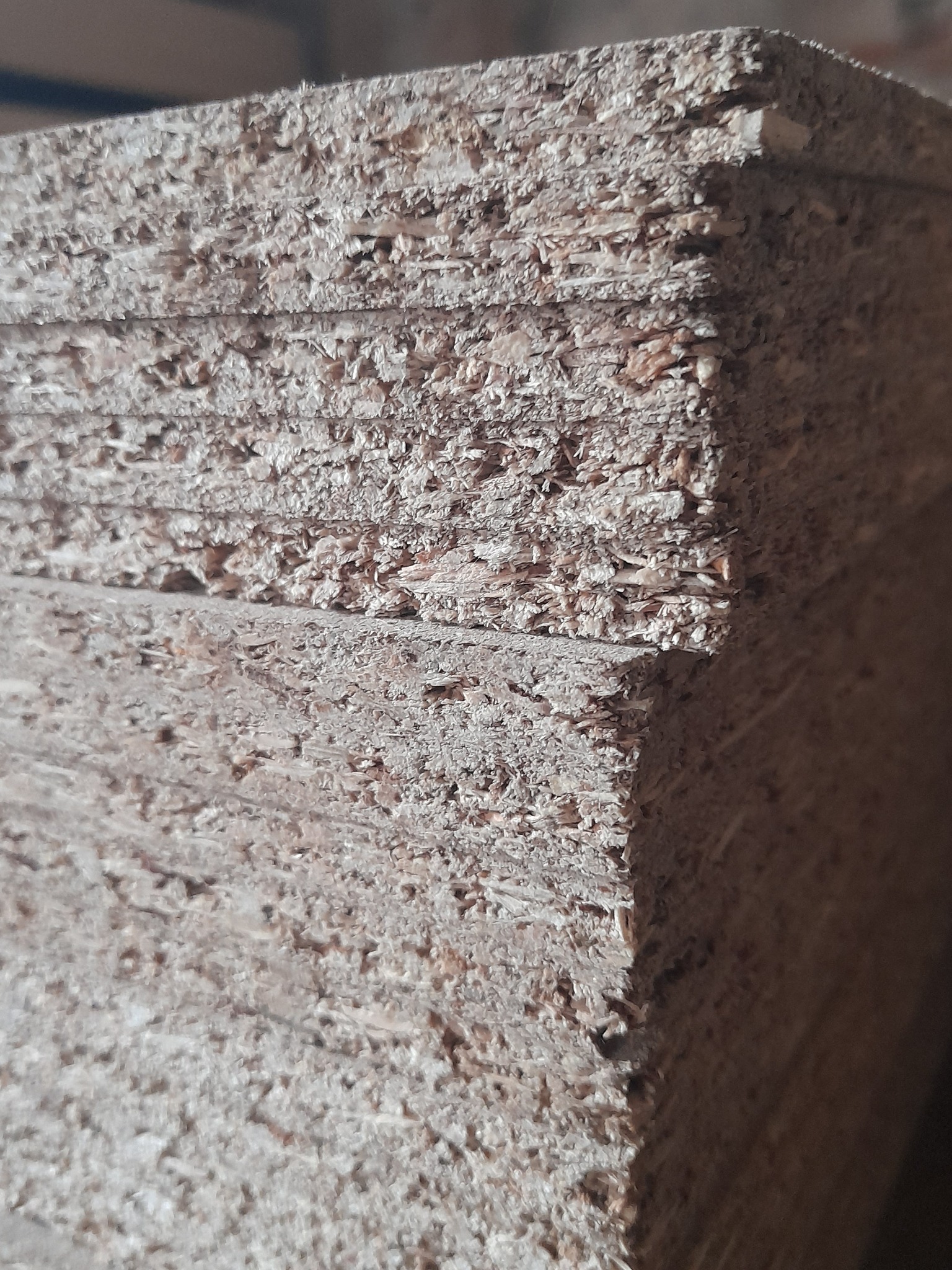 Stos płyt OSB o surowej, widocznej strukturze w magazynie, ukazujący przekrój warstw i nierówności krawędzi.