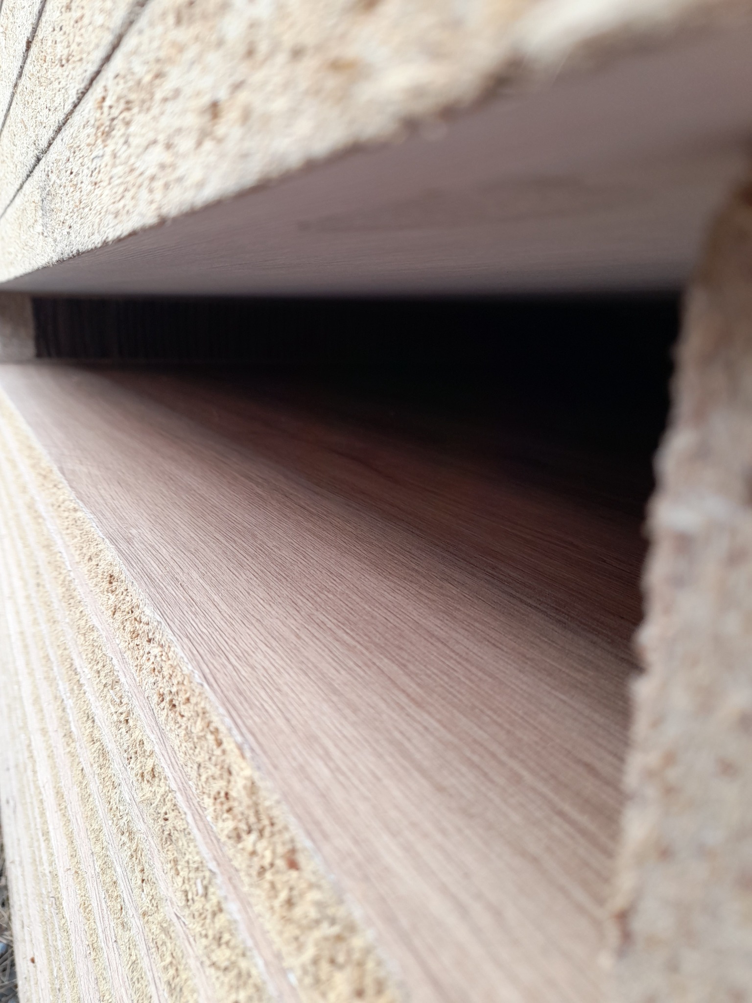 Stos płyt z widoczną strukturą drewna i jasnymi krawędziami z wiórów, ułożonych jeden na drugim.