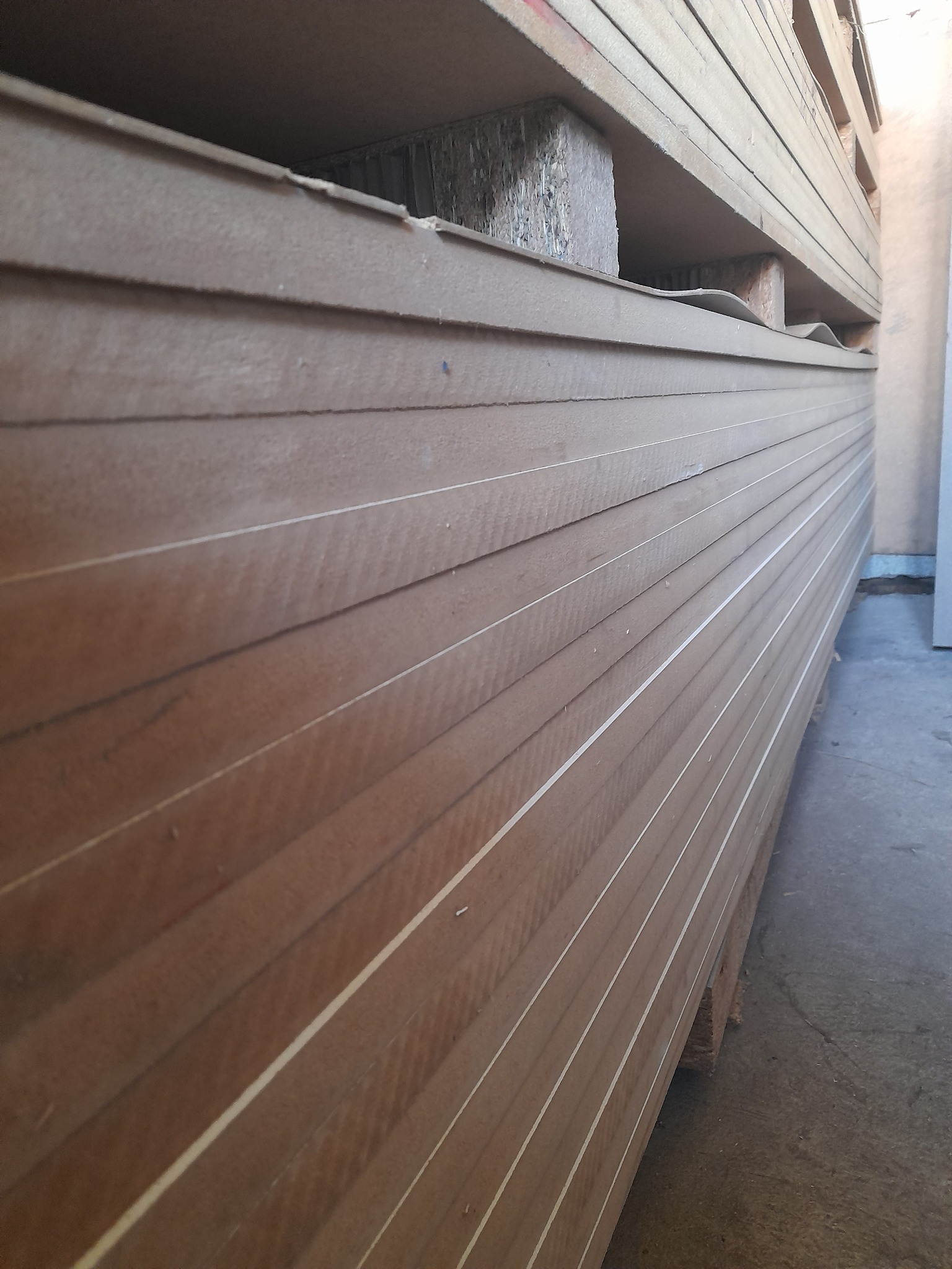 Stos płyt drewnopochodnych, przekładki z płyty wiórowej, widok z dołu pod kątem, magazyn.