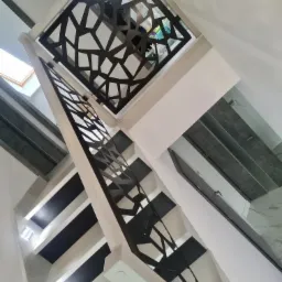 Nowoczesna klatka schodowa z balustradą o geometrycznym wzorze, widok z dołu, białe ściany, czarne stopnie, jasne oświetlenie.