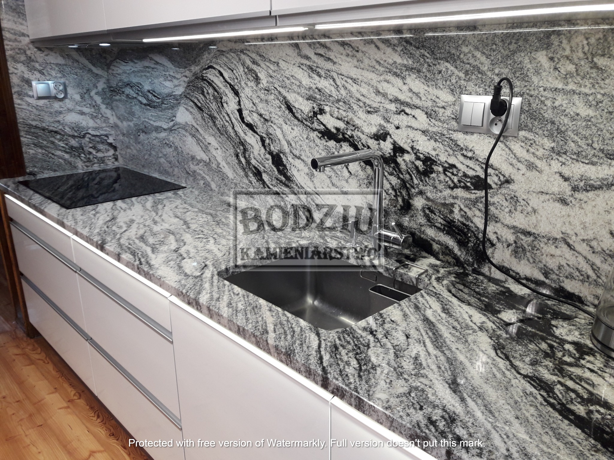 Kuchnia z blatem z kamienia naturalnego o unikalnym wzorze, chromowana bateria, płyta indukcyjna i białe, lakierowane szafki podświetlone listwą LED.