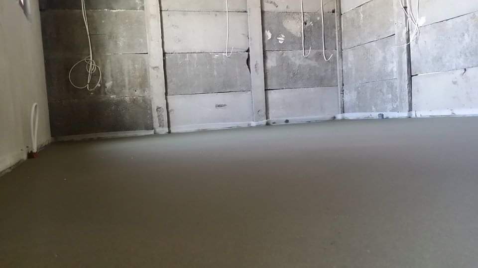 Świeżo wylana, gładka posadzka jastrychowa w surowym wnętrzu z betonowymi ścianami i wiszącymi kablami.