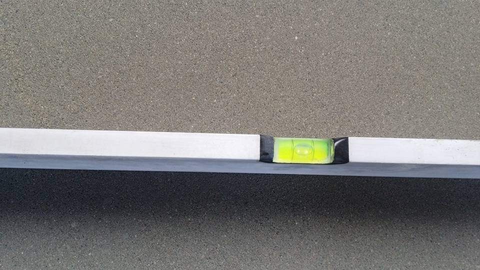 Poziomica aluminiowa z libelką wskazującą poziom na surowej, szorstkiej powierzchni jastrychu.