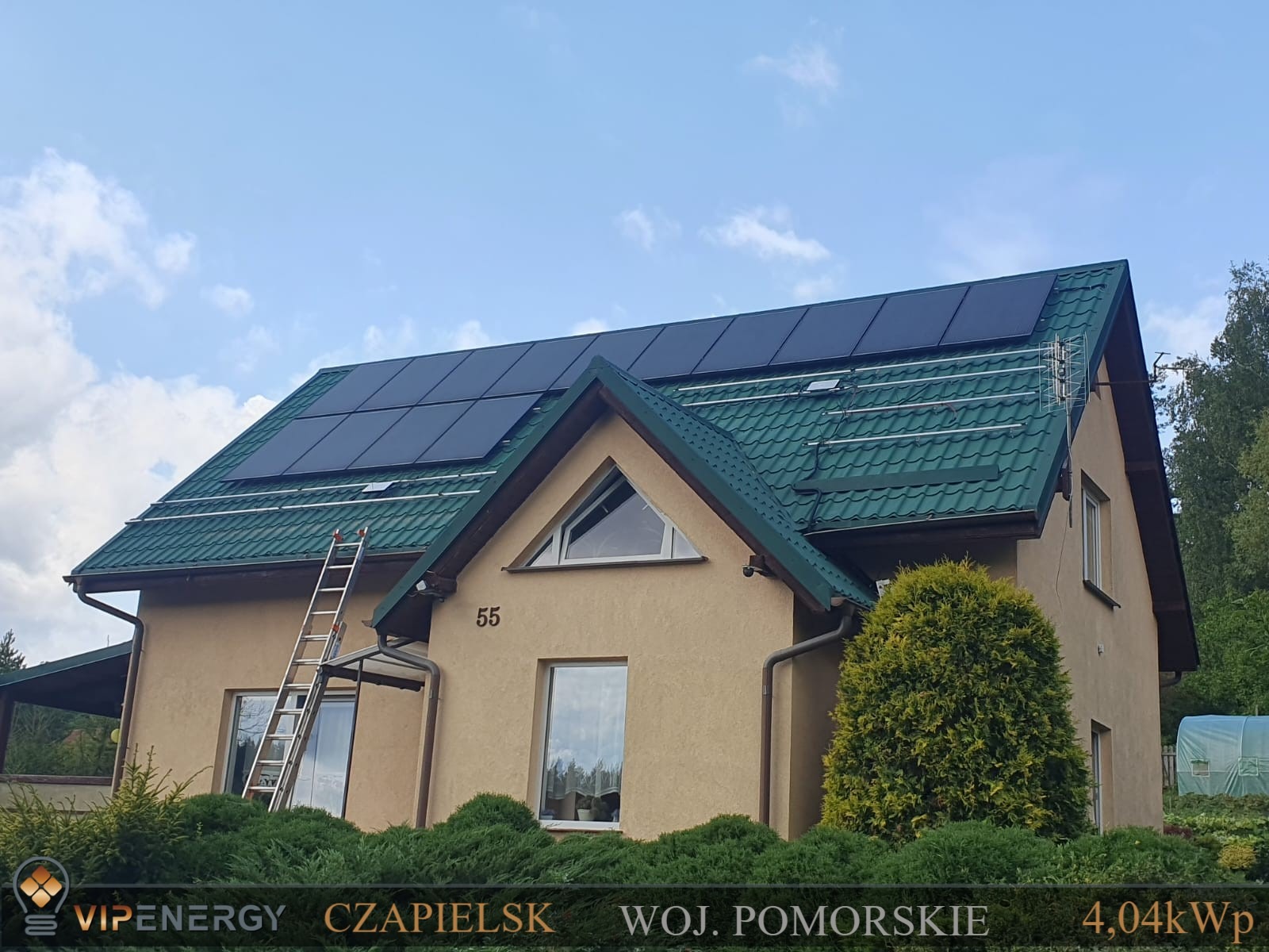 Dom jednorodzinny z zielonym dachem z panelami słonecznymi, drabina oparta o dach, widoczny numer domu 55, logo firmy w dolnej części kadru.
