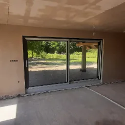 Pokój po tynkowaniu maszynowym z widocznymi przewodami elektrycznymi wystającymi z sufitu oraz śladami po taśmie malarskiej na podłodze.