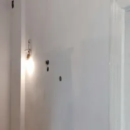 Świeżo położona biała gładź na ścianie z widocznymi otworami na gniazdka elektryczne i niedokończoną podłogą w remontowanym pomieszczeniu.