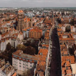 Panoramiczny widok z lotu ptaka na Gdańsk z dominującą ceglaną architekturą i czerwonymi dachami, ukazujący perspektywę ulic i Starego Miasta w pochmurny dzień.