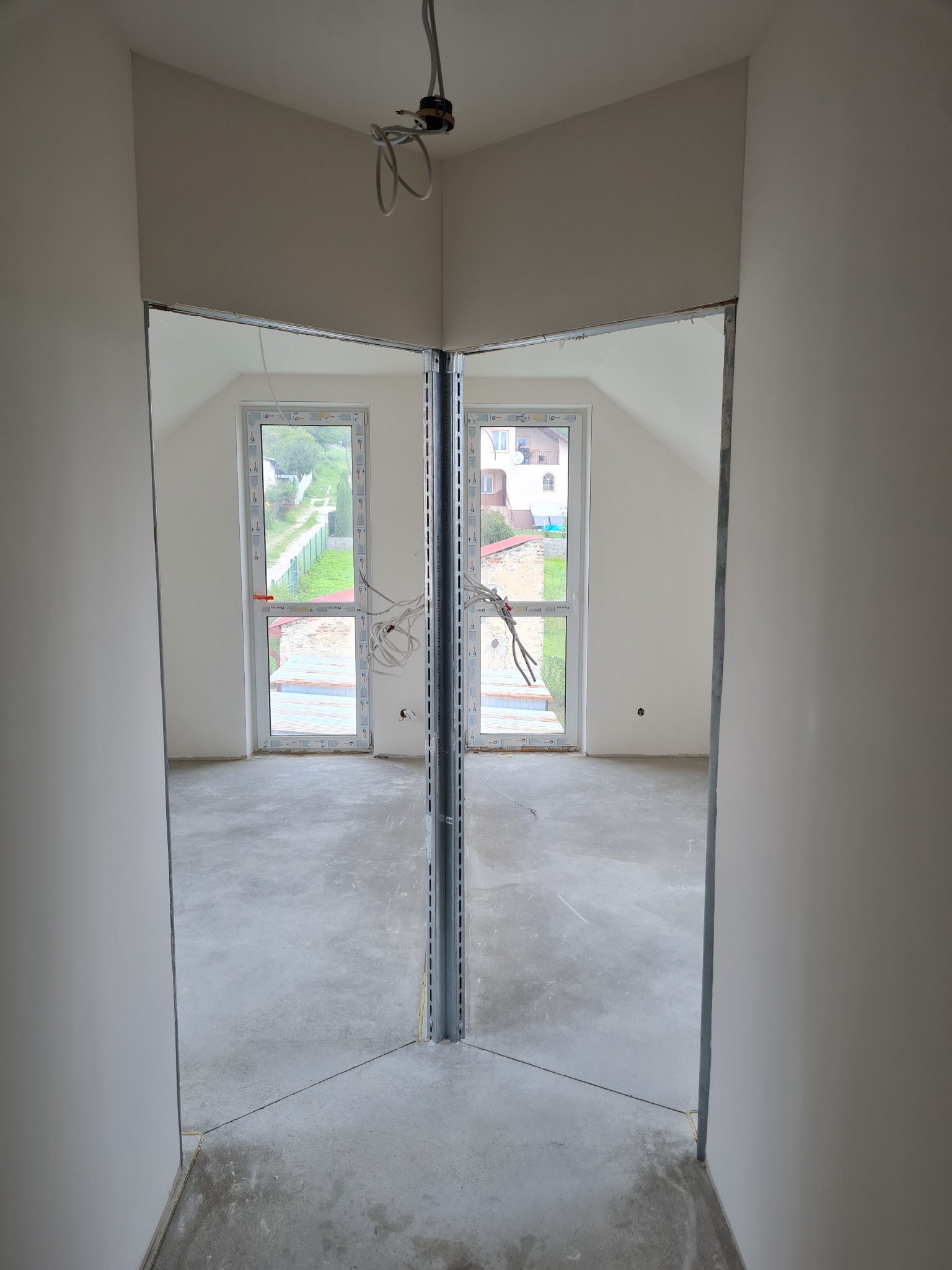 Wnętrze w trakcie prac wykończeniowych, widoczne profile metalowe tworzące ramy ścian działowych i przygotowane podłoże pod posadzkę, okna dachowe z widokiem na zewnątrz.