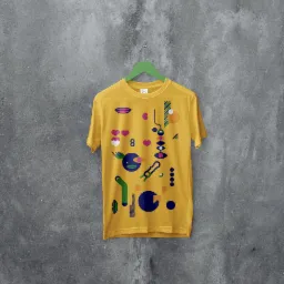 Żółta koszulka z abstrakcyjnym, geometrycznym nadrukiem w kolorach niebieskim, zielonym, pomarańczowym i różowym, zawieszona na zielonym wieszaku na tle szarej, teksturowanej ściany.