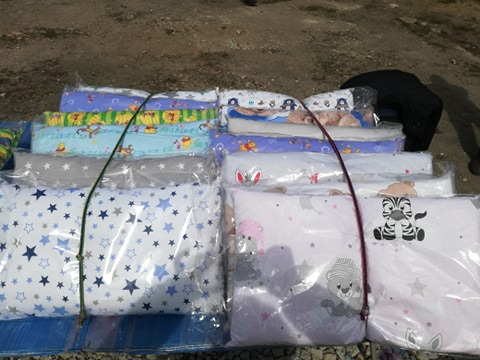 Stosy zapakowanych w folię poduszek i kołderek dziecięcych z różnymi wzorami, takimi jak gwiazdki, zwierzątka i postacie z bajek, zabezpieczone sznurkiem.