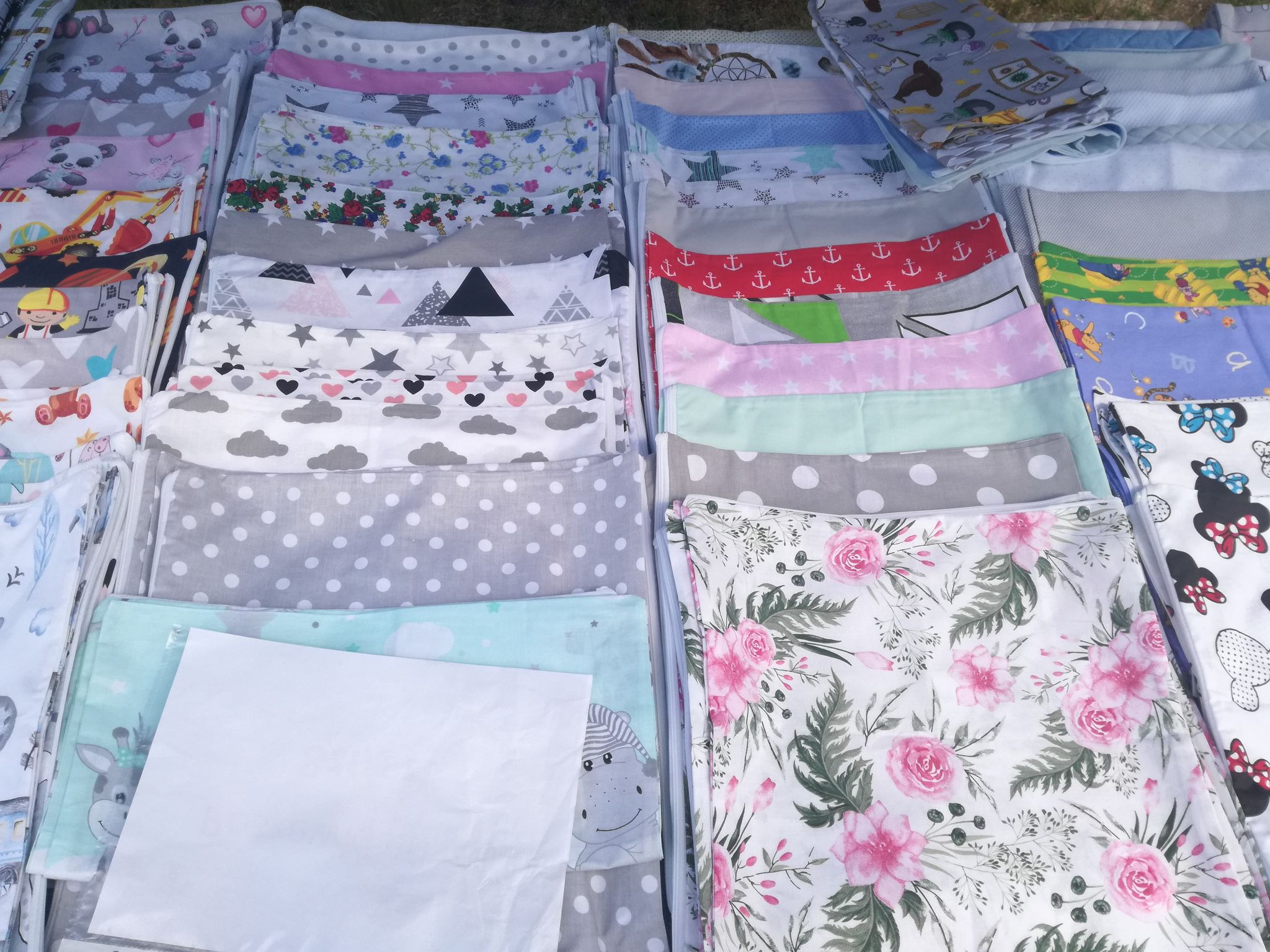 Stosy uszytych poszewek na kołdry i poduszki z różnorodnych wzorzystych tkanin, od dziecięcych motywów po kwiatowe i geometryczne, ułożone równo na wystawie.