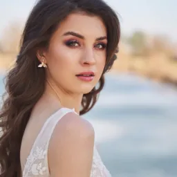Portret panny młodej z profesjonalnym makijażem, podkreślonymi oczami w odcieniach różu i brązu, delikatnymi ustami i upięciem z loków, w koronkowej sukni z odkrytymi ramionami i z kolczykami...