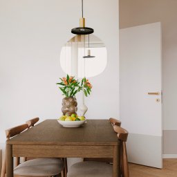 Szyra Studio - Nowoczesna jadalnia z drewnianym stołem, krzesłami z szarą tapicerką, wazonem z pomarańczowymi kwiatami i owocami, oświetlona designerską lampą wiszącą i odbijająca się w okrągłym lustrze na ścianie.