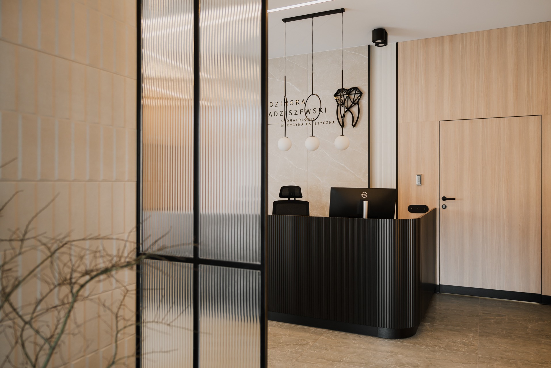 Nowoczesna recepcja w gabinecie stomatologicznym z czarnym biurkiem recepcyjnym, designerską lampą wiszącą i dekoracją ścienną w kształcie zęba.