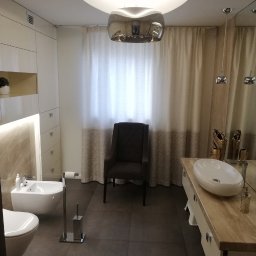 DAM-BUD Damian Saługa - Nowoczesna łazienka z ciemnymi płytkami podłogowymi, białymi sanitariatami, kremowymi zasłonami i designerską lampą wiszącą.