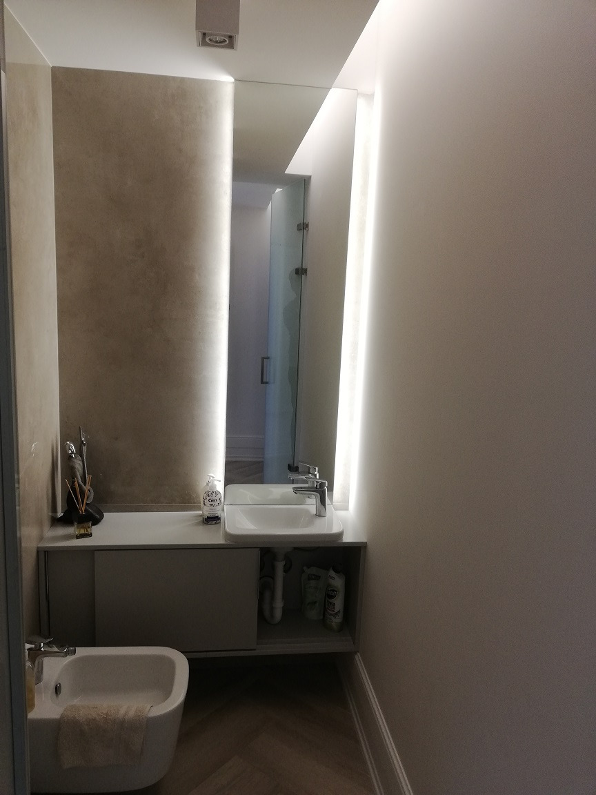 Nowoczesna łazienka z podświetlanym lustrem, umywalką nablatową i bidetem, wykończona w jasnych odcieniach szarości i bieli, z podłogą w jodełkę.