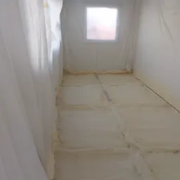 Poddasze zabezpieczone folią malarską z widoczną warstwą natryśniętej pianki PUR na podłodze, tworzącej izolację termiczną.