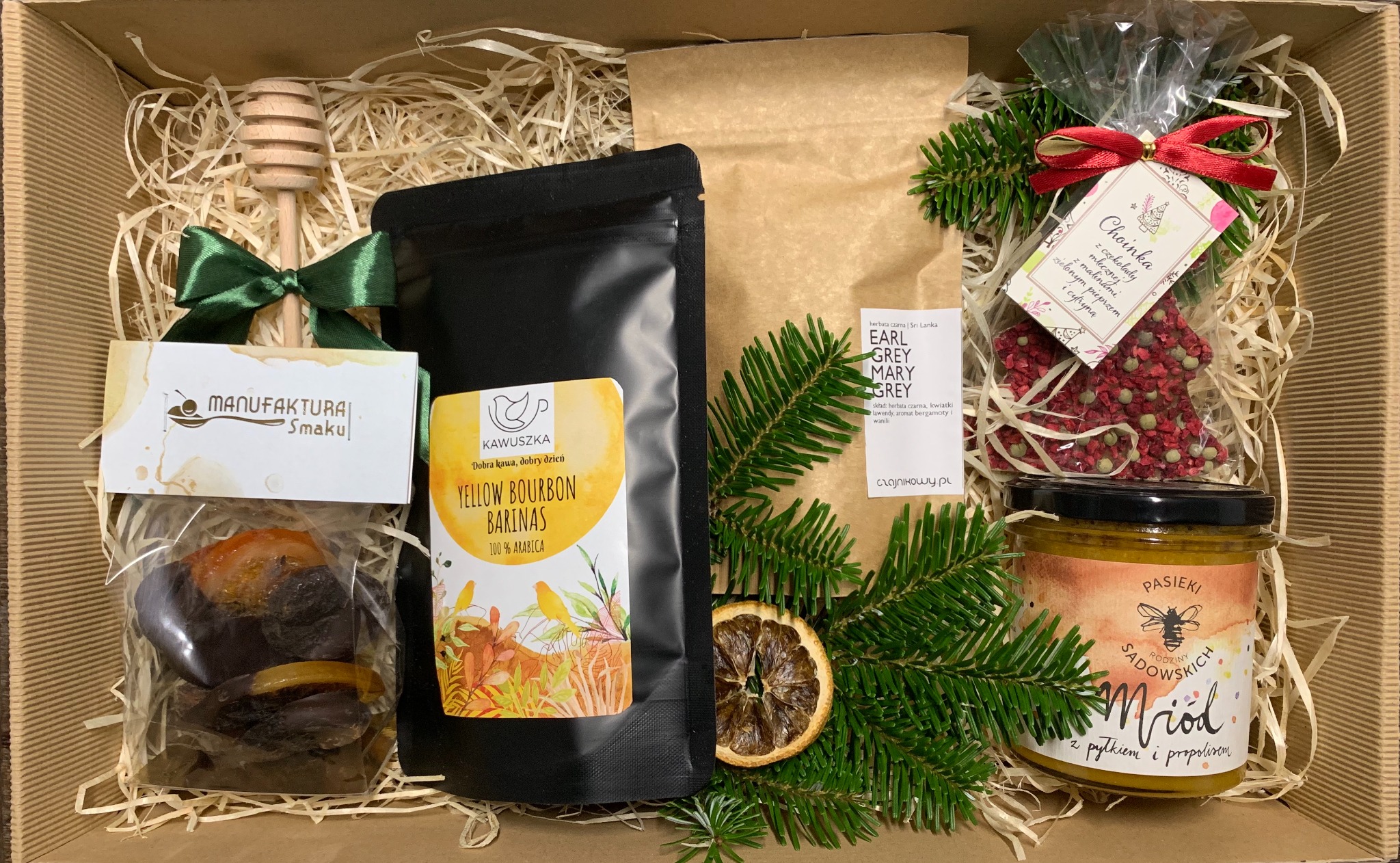 Otwarty kartonowy box wypełniony siankiem, zawierający zestaw upominkowy: miód z pyłkiem i propolisem w słoiku, paczkę kawy Yellow Bourbon Barinas, herbatę Earl Grey Mary Grey, czekoladę...