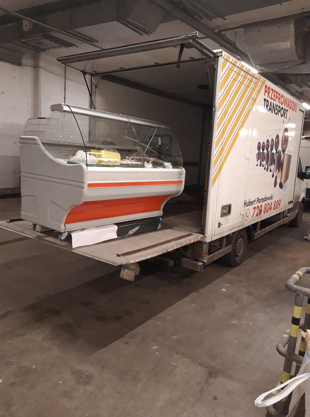 Chłodnicza witryna sklepowa umieszczona na platformie samochodu dostawczego firmy transportowej z Torunia, przygotowana do przewozu.