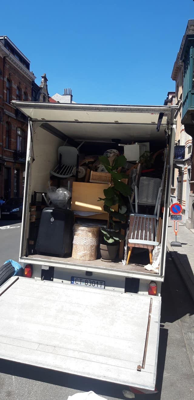Otwarta paka busa wypełniona meblami, kartonami i roślinami doniczkowymi podczas dnia przeprowadzkowego na tle zabudowy miejskiej.
