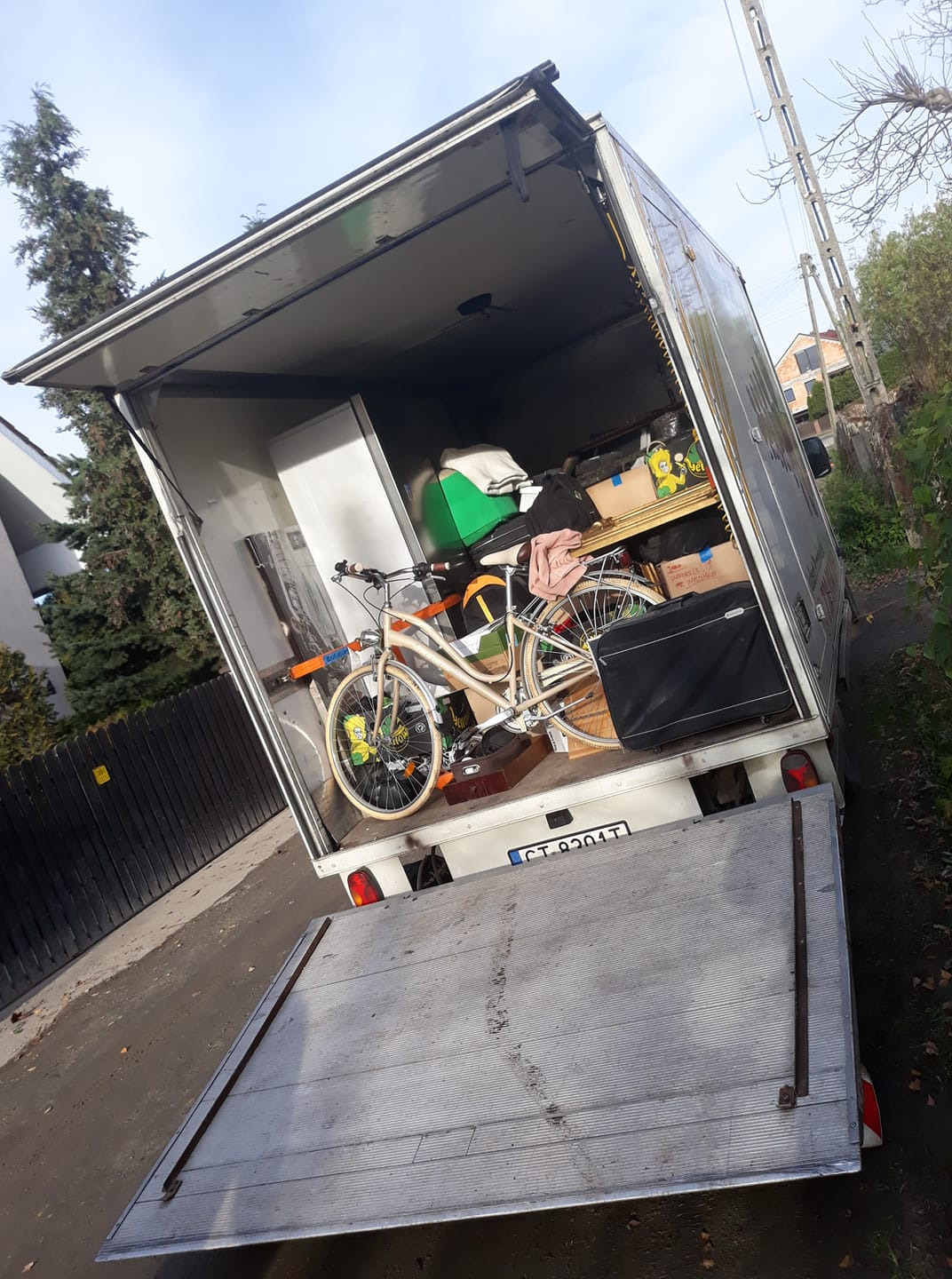 Otwarta paka samochodu dostawczego, wypełniona meblami, kartonami i rowerem, gotowa do transportu.