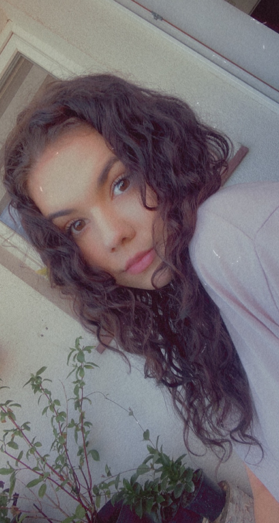 Portret młodej kobiety z kręconymi włosami w Płocku, z rośliną doniczkową w tle, wykonany w miękkim oświetleniu.