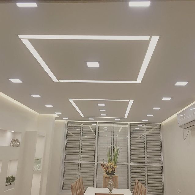 Nowoczesny sufit podwieszany z oświetleniem LED w kształcie kwadratów, widok na jadalnię z oknem i klimatyzacją. Minimalistyczny design.