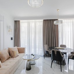 Michał Ziędalski - Jasny salon z beżową sofą z poduszkami, okrągłym stołem jadalnym z czarnym blatem i marmurową podłogą