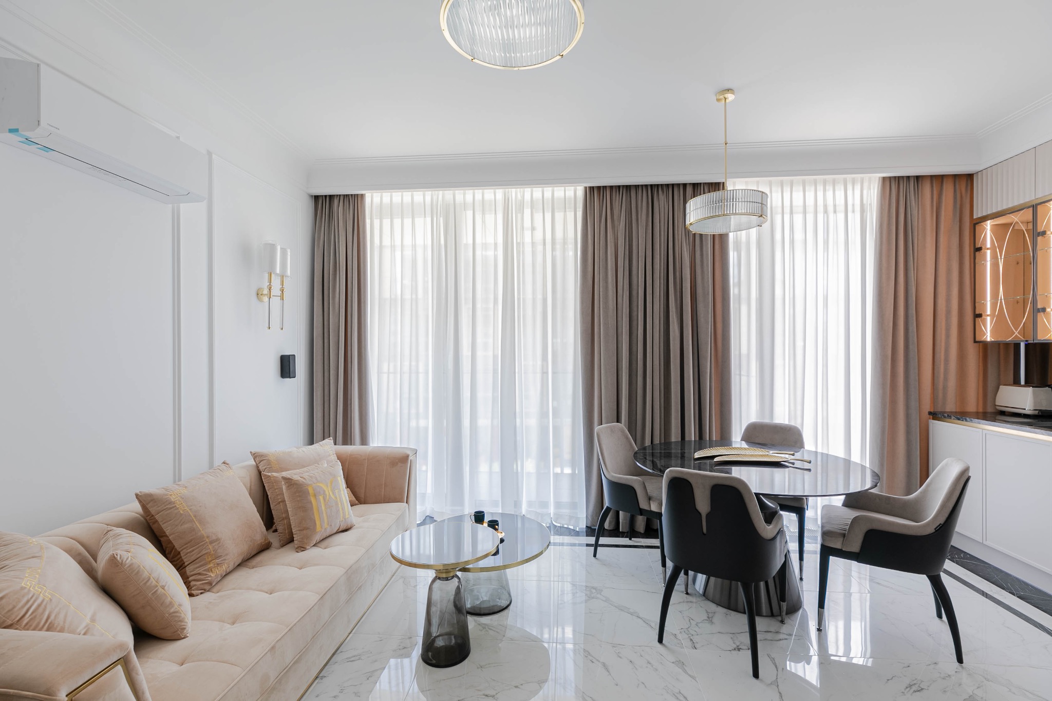 Jasny salon z beżową sofą z poduszkami, okrągłym stołem jadalnym z czarnym blatem i marmurową podłogą