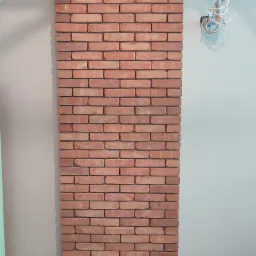 Panel ścienny z cegieł klinkierowych w odcieniach czerwieni i brązu, zamontowany na ścianie w pomieszczeniu w trakcie wykończenia, widoczne instalacje elektryczne na ścianie.