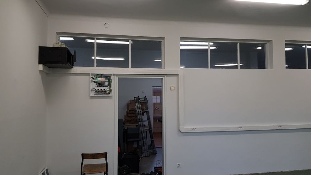 Zamontowana skrzynka elektryczna i czarna obudowa szafy teletechnicznej na ścianie w pomieszczeniu z oknami, widoczna drabina i narzędzia.