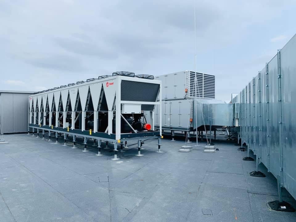 Rozległy system klimatyzacji przemysłowej z wieloma jednostkami zewnętrznymi na płaskim dachu, widoczne kanały wentylacyjne i anteny.