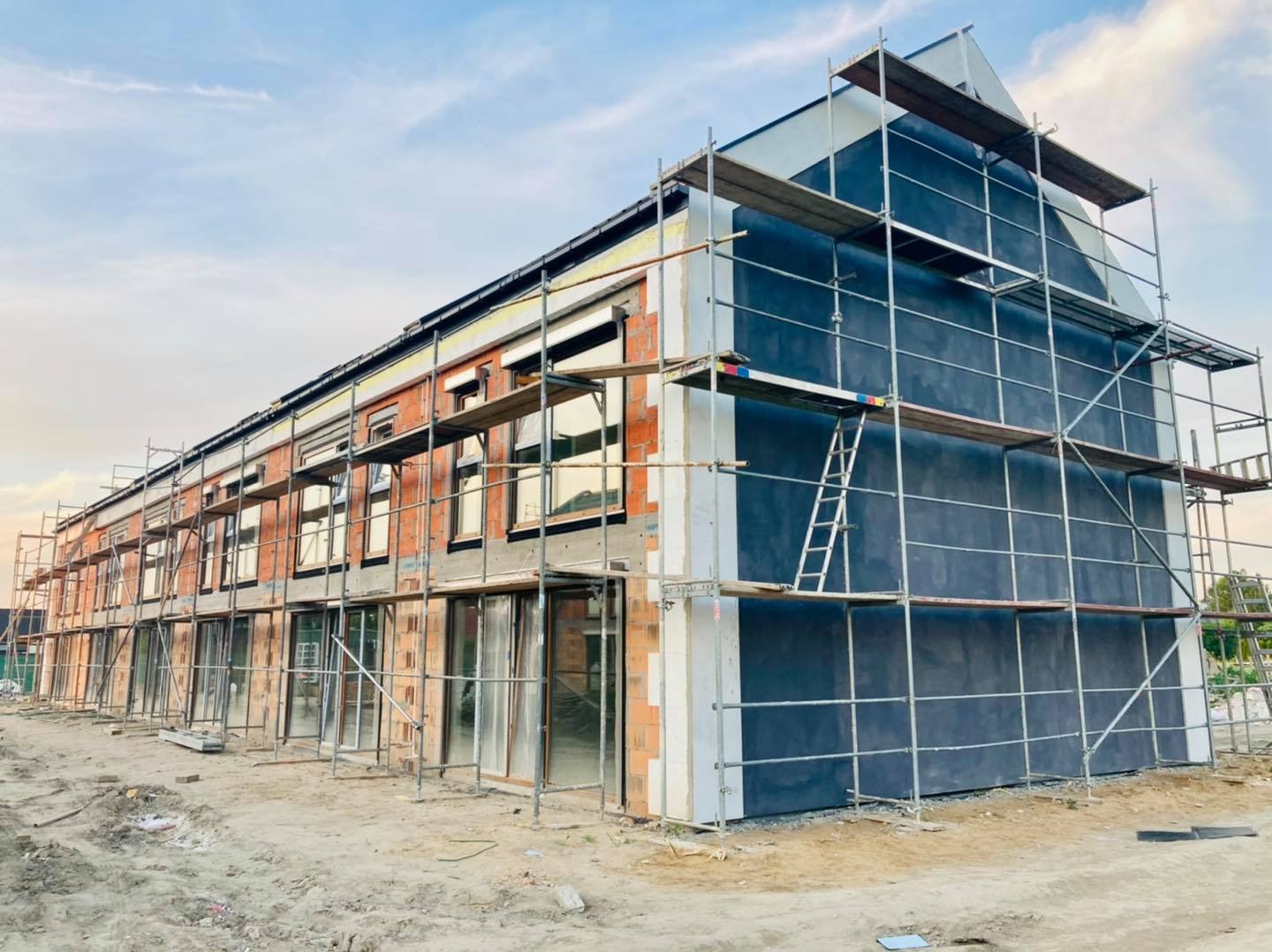 Budynek wielorodzinny w trakcie ocieplania, widoczne rusztowania, warstwa izolacyjna na ścianach i okna wstawione w surowym murze.