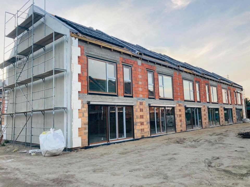 Budowa szeregowca w trakcie: surowa cegła, okna wstawione, ocieplenie styropianem, rusztowanie przy elewacji, dach pokryty papą.