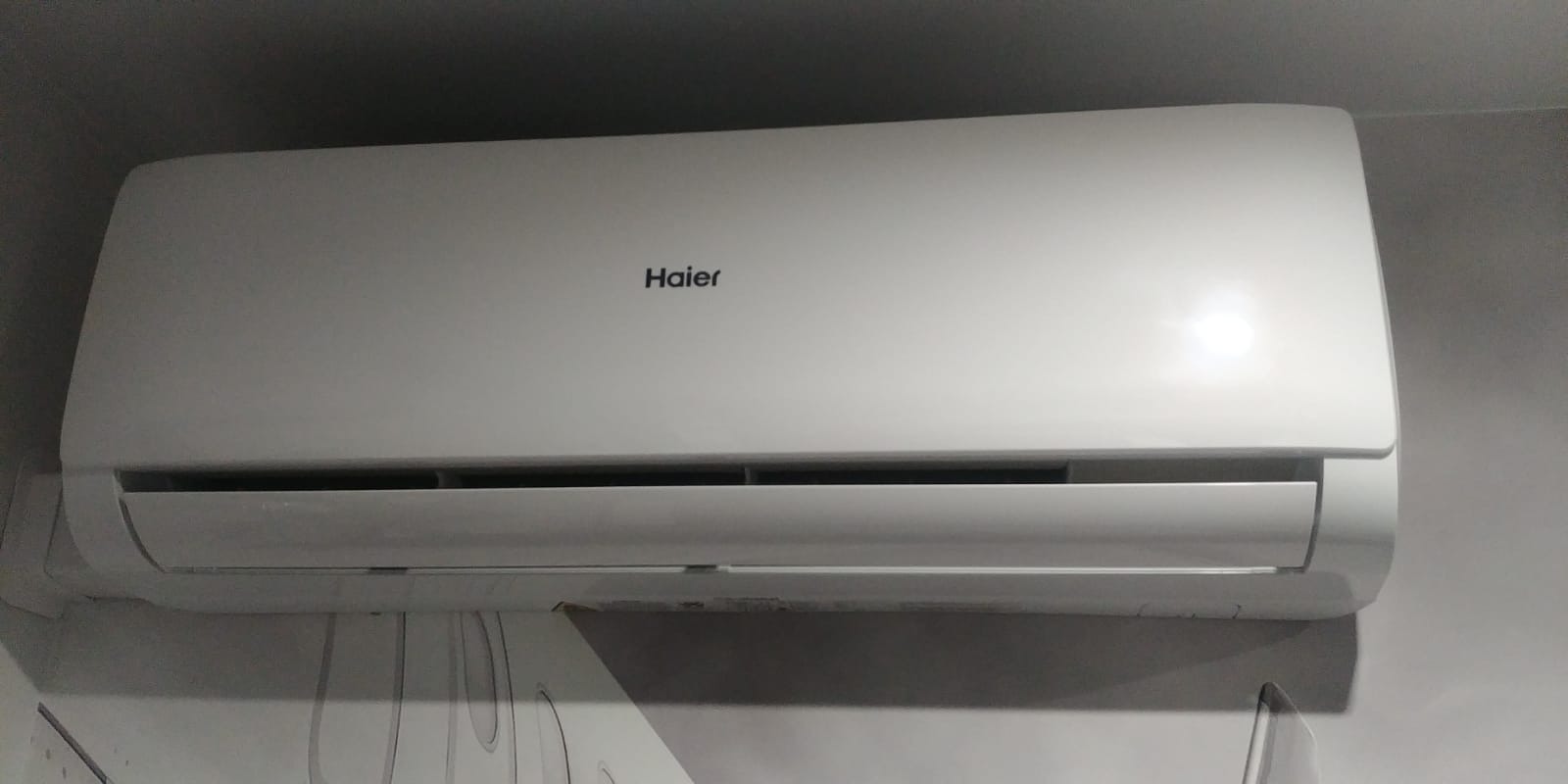 Biała jednostka klimatyzacji Haier zamontowana na ścianie z delikatnym wzorem, widoczna pod kątem od dołu.