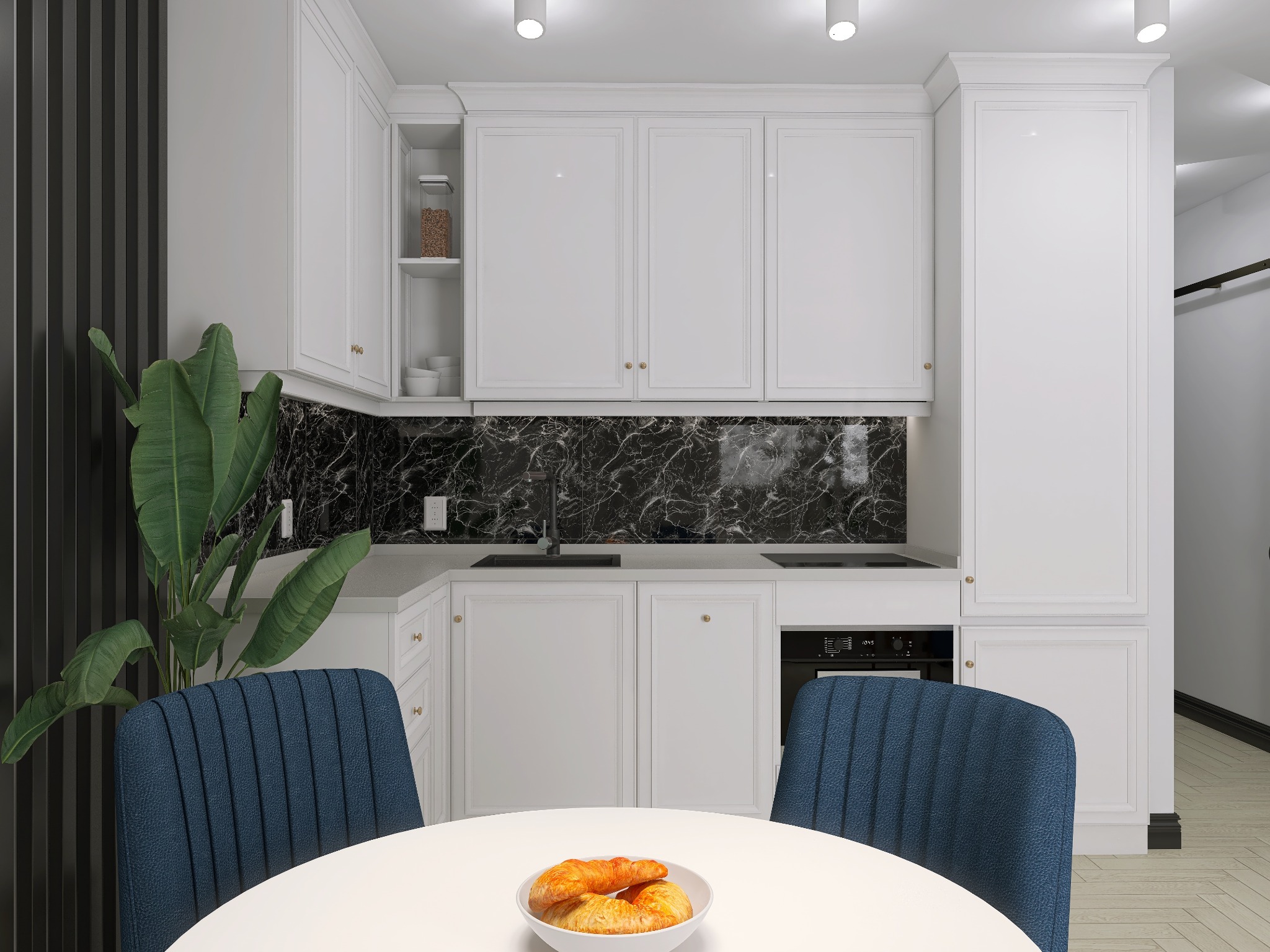 Nowoczesna kuchnia z białymi szafkami, czarnym marmurowym backsplashiem i okrągłym białym stołem z niebieskimi krzesłami oraz miską z croissantami na pierwszym planie.