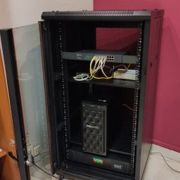 Streampc Serwis - Otwarta szafa rack z zainstalowanym routerem TP-Link, switchem, serwerem DellEMC i zasilaczem awaryjnym Volt Polska, widoczne okablowanie.