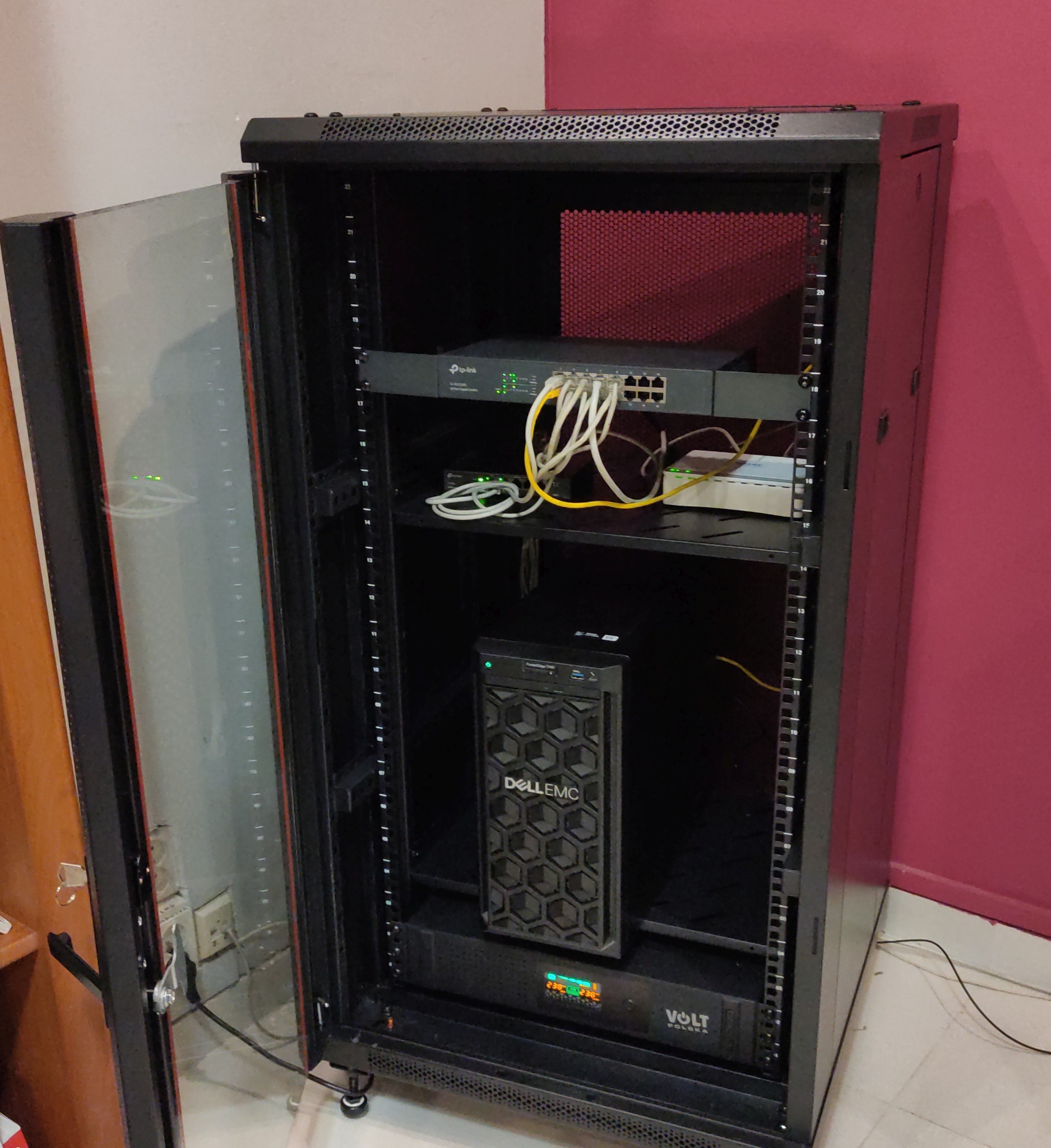 Otwarta szafa rack z zainstalowanym routerem TP-Link, switchem, serwerem DellEMC i zasilaczem awaryjnym Volt Polska, widoczne okablowanie.
