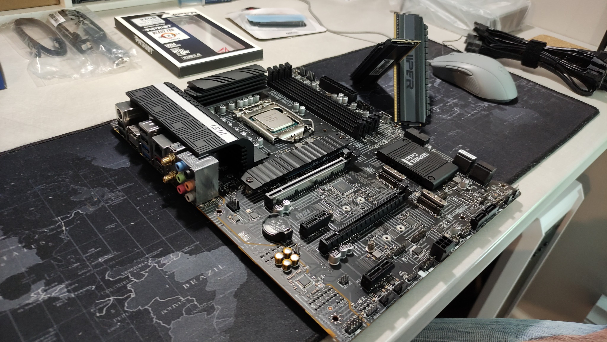 Płyta główna MSI Pro Series z zainstalowanym procesorem Intel, pamięcią RAM Viper i akcesoriami na podkładce z mapą świata, przygotowana do instalacji w obudowie komputera.