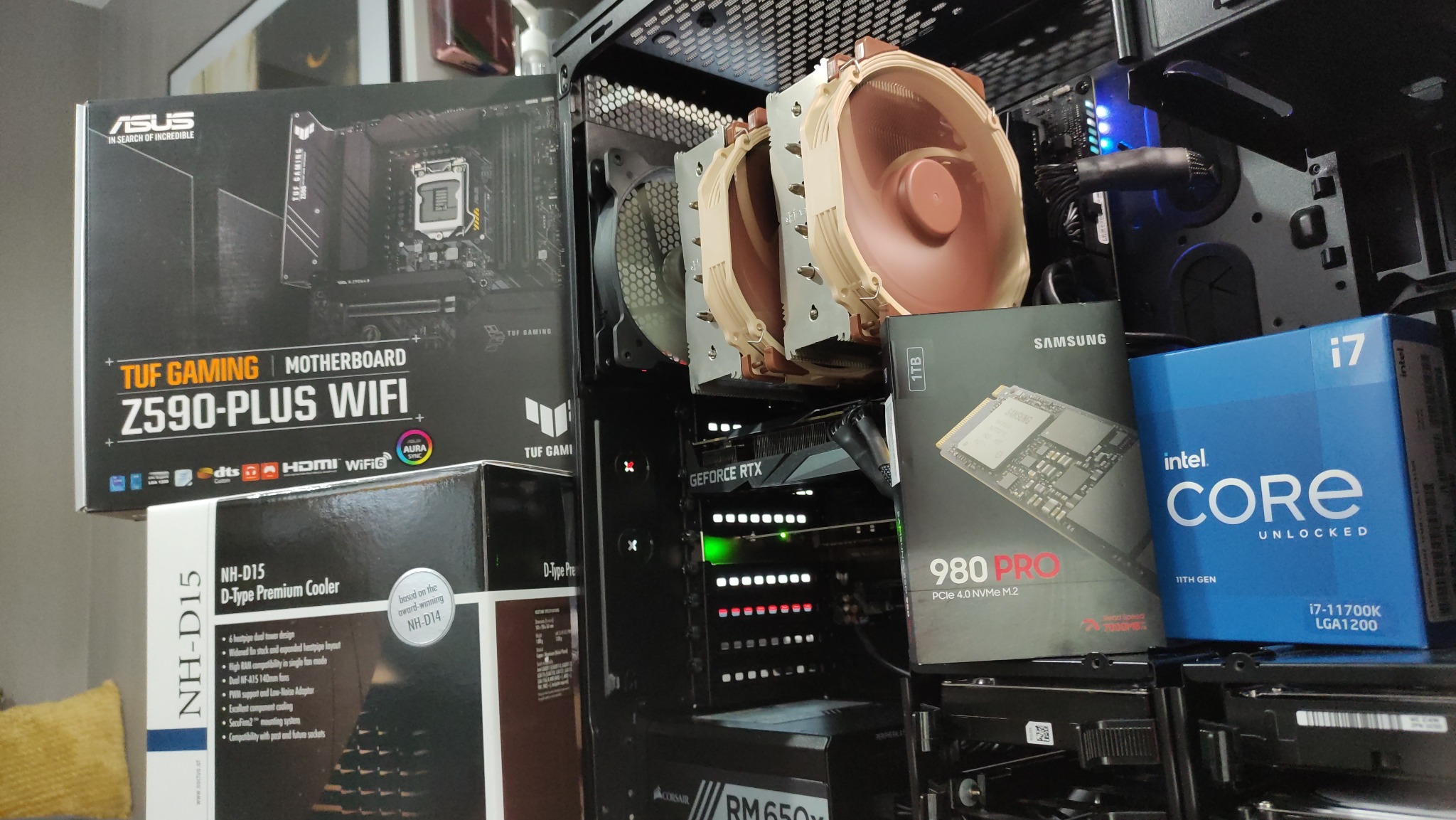 Wnętrze obudowy komputera stacjonarnego z zamontowanymi komponentami, takimi jak karta graficzna GeForce RTX, chłodzenie procesora Noctua NH-D15, dysk SSD Samsung 980 PRO oraz pudełka po płycie...