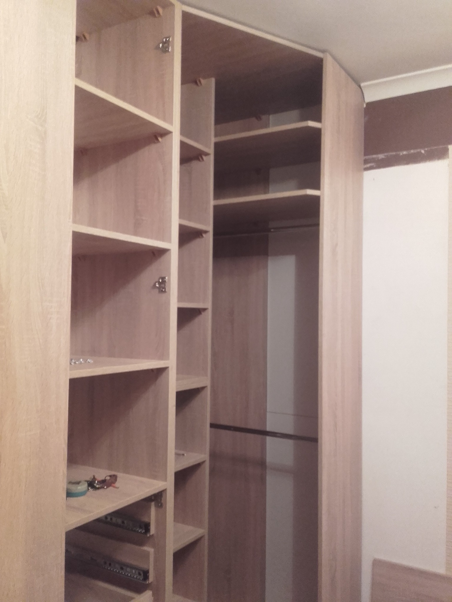 Wnętrze szafy wnękowej z jasnego drewna, widoczne półki, szuflady na prowadnicach i drążek na ubrania, montaż w trakcie wykańczania wnętrza.