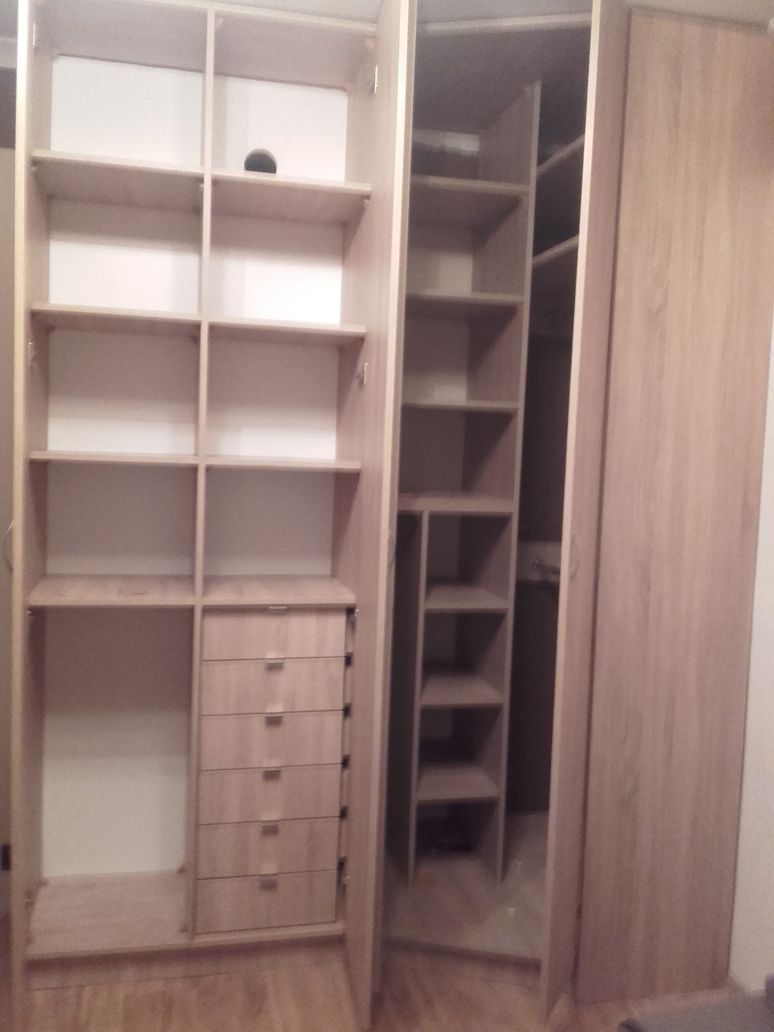 Otwarta szafa wnękowa z jasnego drewna z półkami i szufladami, widoczna konstrukcja z podziałem na strefy.