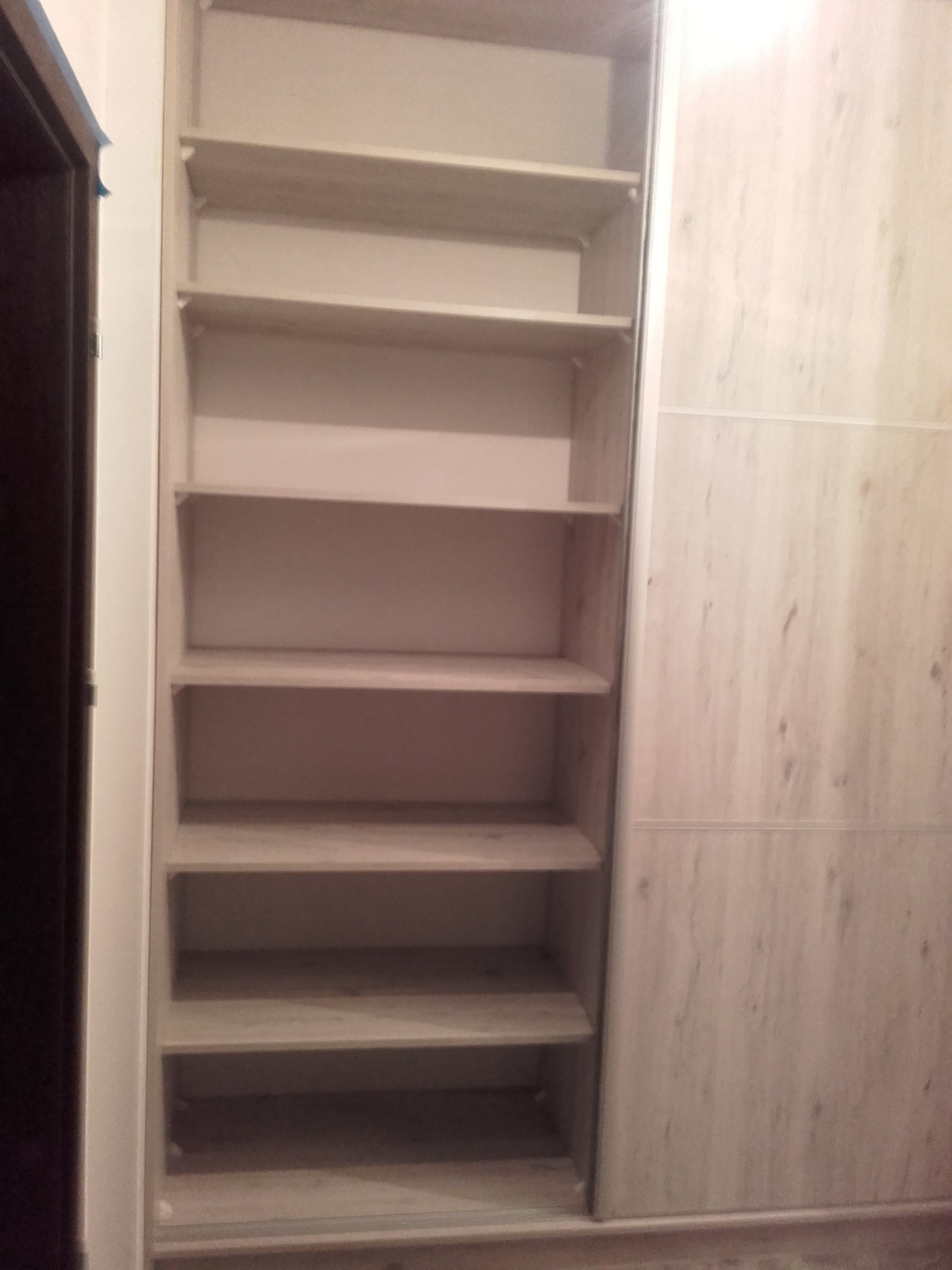 Wnętrze szafy wnękowej z jasnego drewna, z półkami, wykonanej na zamówienie w Radomsku, widoczne przesuwne drzwi.