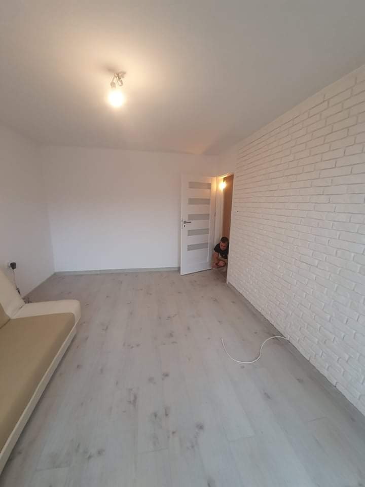 Jasne, odnowione wnętrze z sofą, białą ścianą z cegły i dzieckiem wyglądającym zza otwartych drzwi.